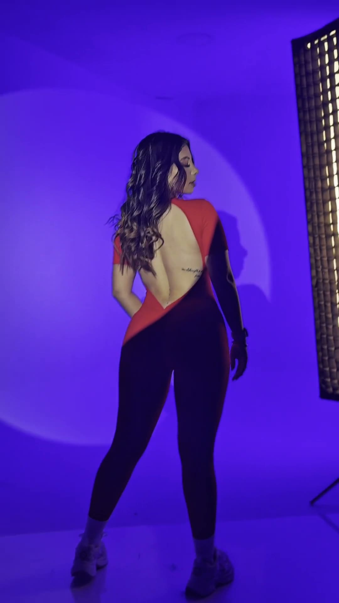 Modelo de espaldas luciendo un enterizo deportivo rojo y negro de Hecho con Amor, en estudio con luz violeta